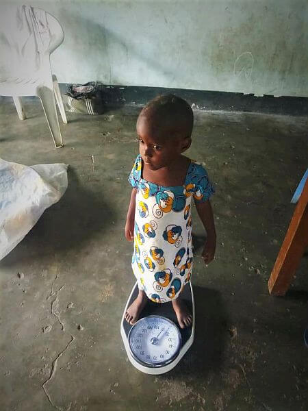 Bambina piccola africana in piedi sulla bilancia della mensa