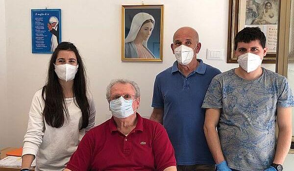 Quattro volontari con mascherine davanti al quadro della Madonna nella sede dell'Associazione Madre Teresa di Calcutta Onlus