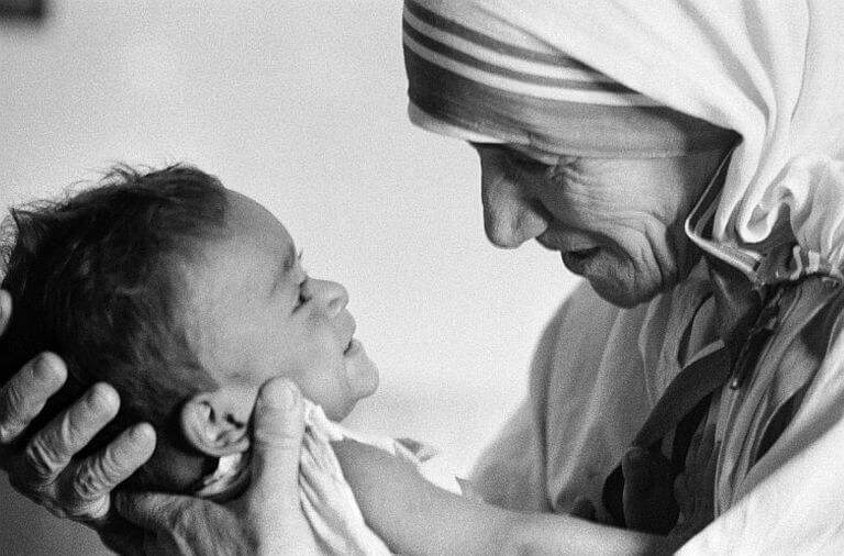 Madre Teresa tiene in braccio con amore un bambino piccolo sorridente